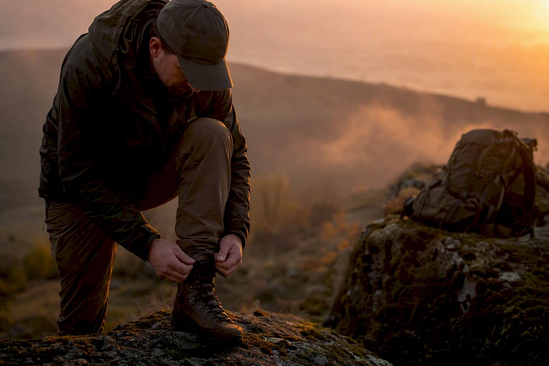 Hunter tying tactical boots outdoors at dawn