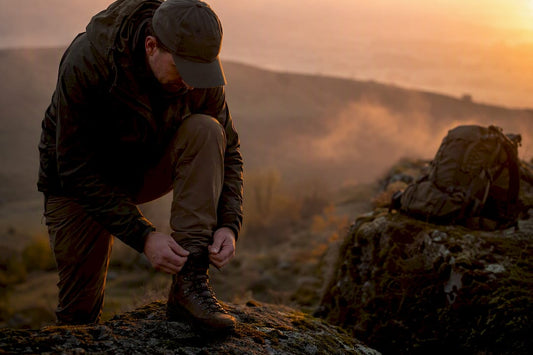 Hunter tying tactical boots outdoors at dawn